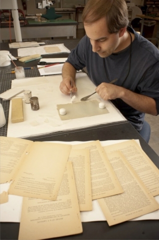 A curator works at a table repairing a book.