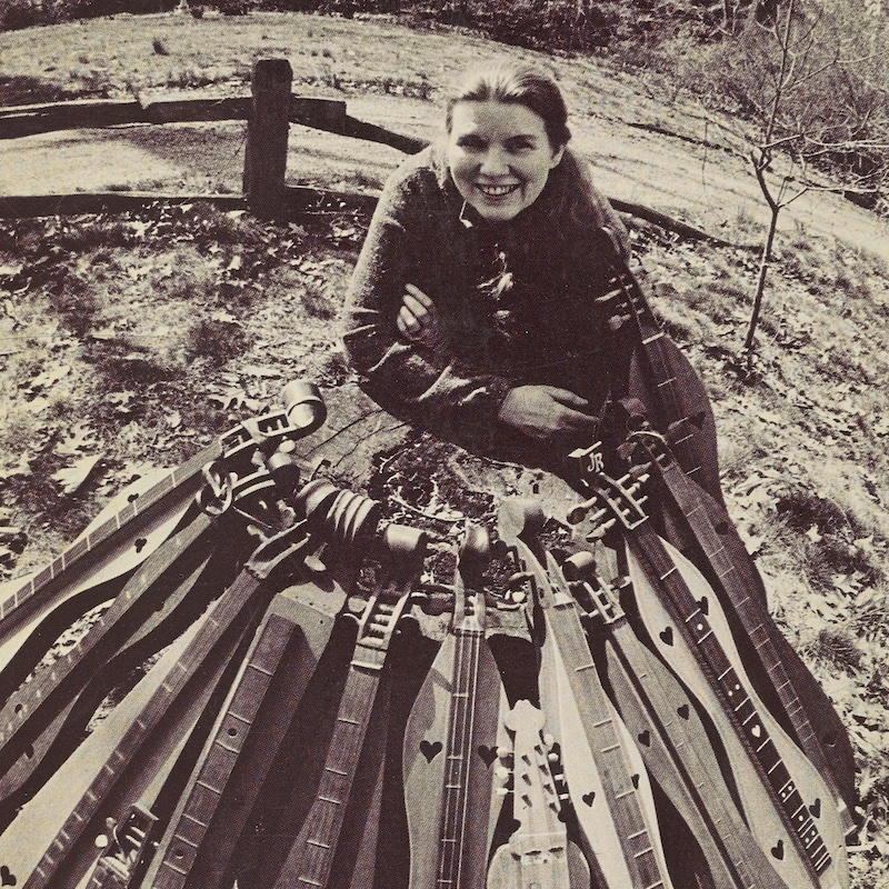 ack and white photograph of Jean Ritchie outdoors with dulcimers, from Ritchie’s book Dulcimer People, 1975. 