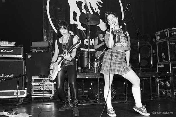 Black and white photo of the band Bikini Kill and Joan Jett performing onstage.