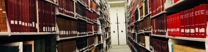 A view down an aisle of twelve-foot high library shelving full of colorful bound volumes.