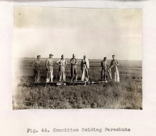 black and white photo of 7 men standing in a field captioned "Fig. 44. Committee Holding Parachute"