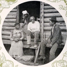 Photo of several people sitting outside a log cabin.